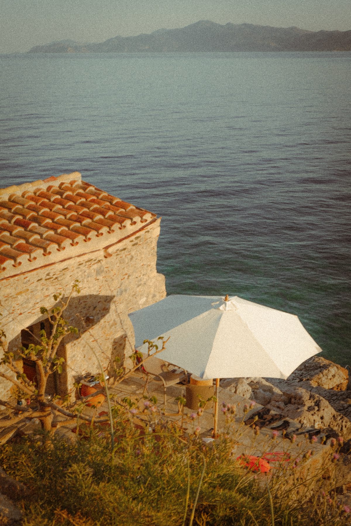 Terrace with a cream parasol on the rocks above the sea at golden hour