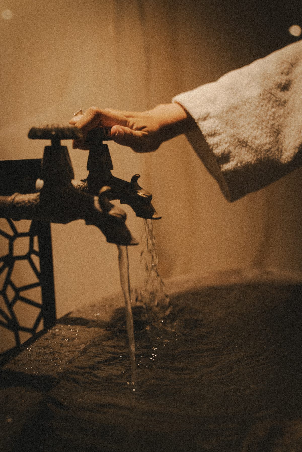 A hand turning an old iron tap, water running into a stone basin