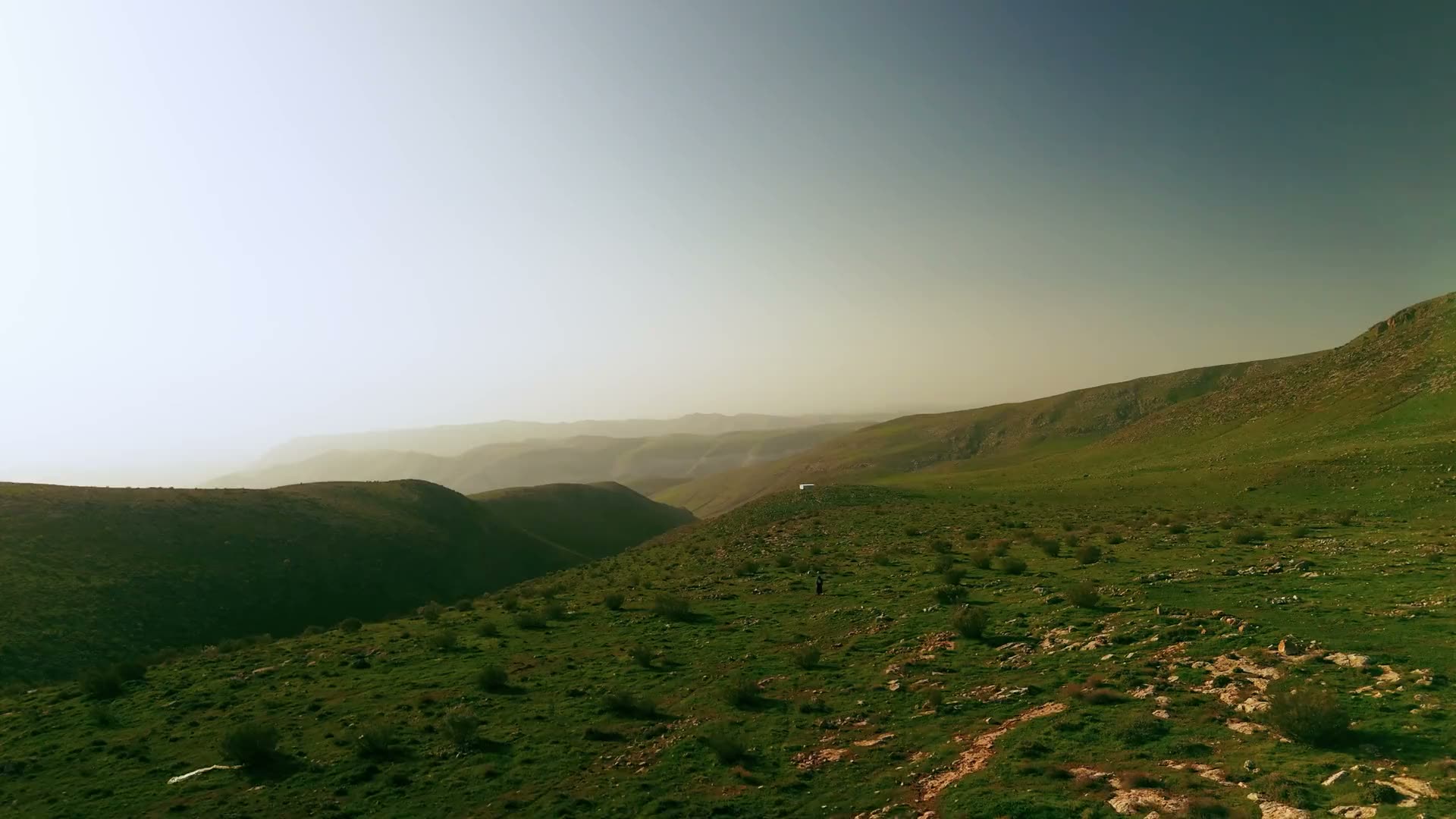Aerial view over green hills at dusk, haze settling on the ridges beyond.